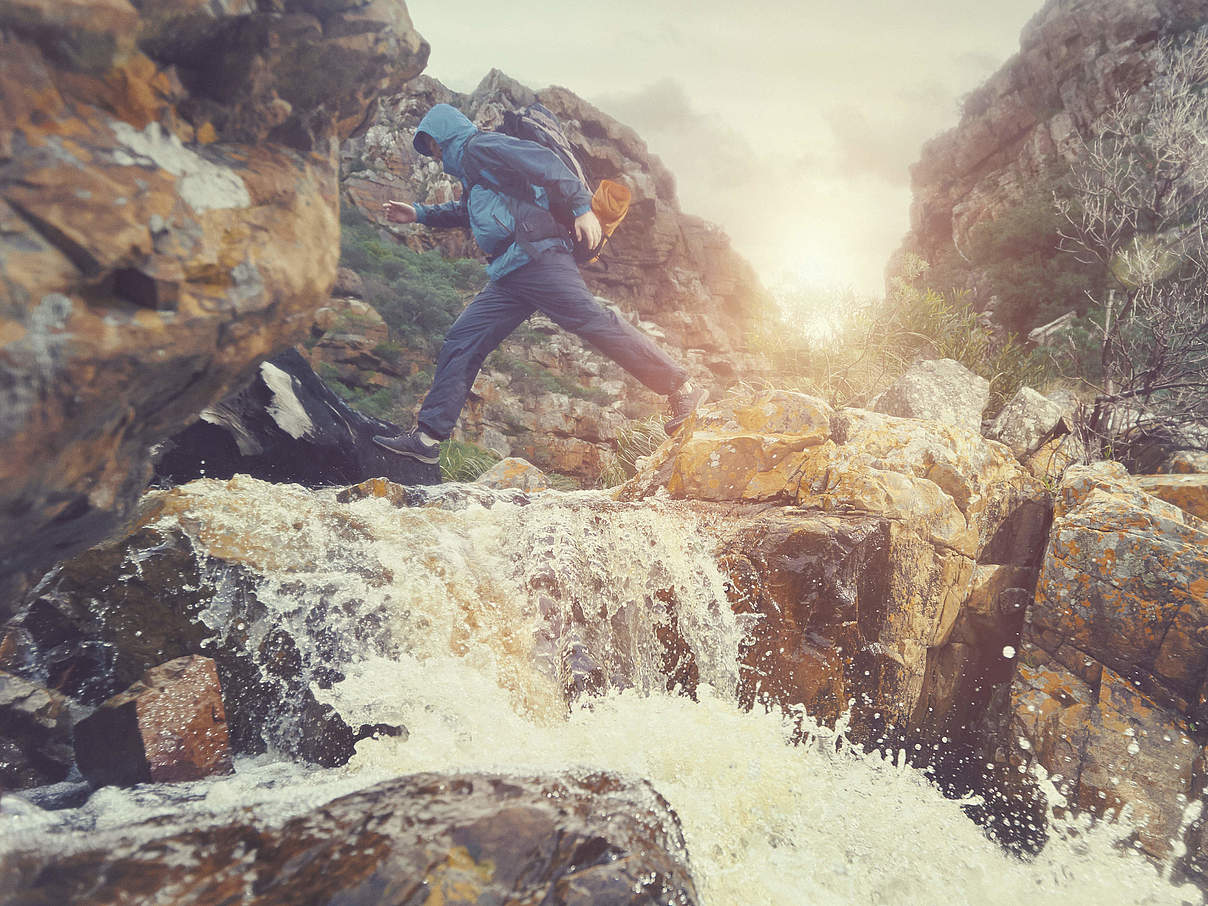 Mensch klettert über Steine an einem Wasserfall © Warren Goldswain / Getty Images / iStockphoto / WWF