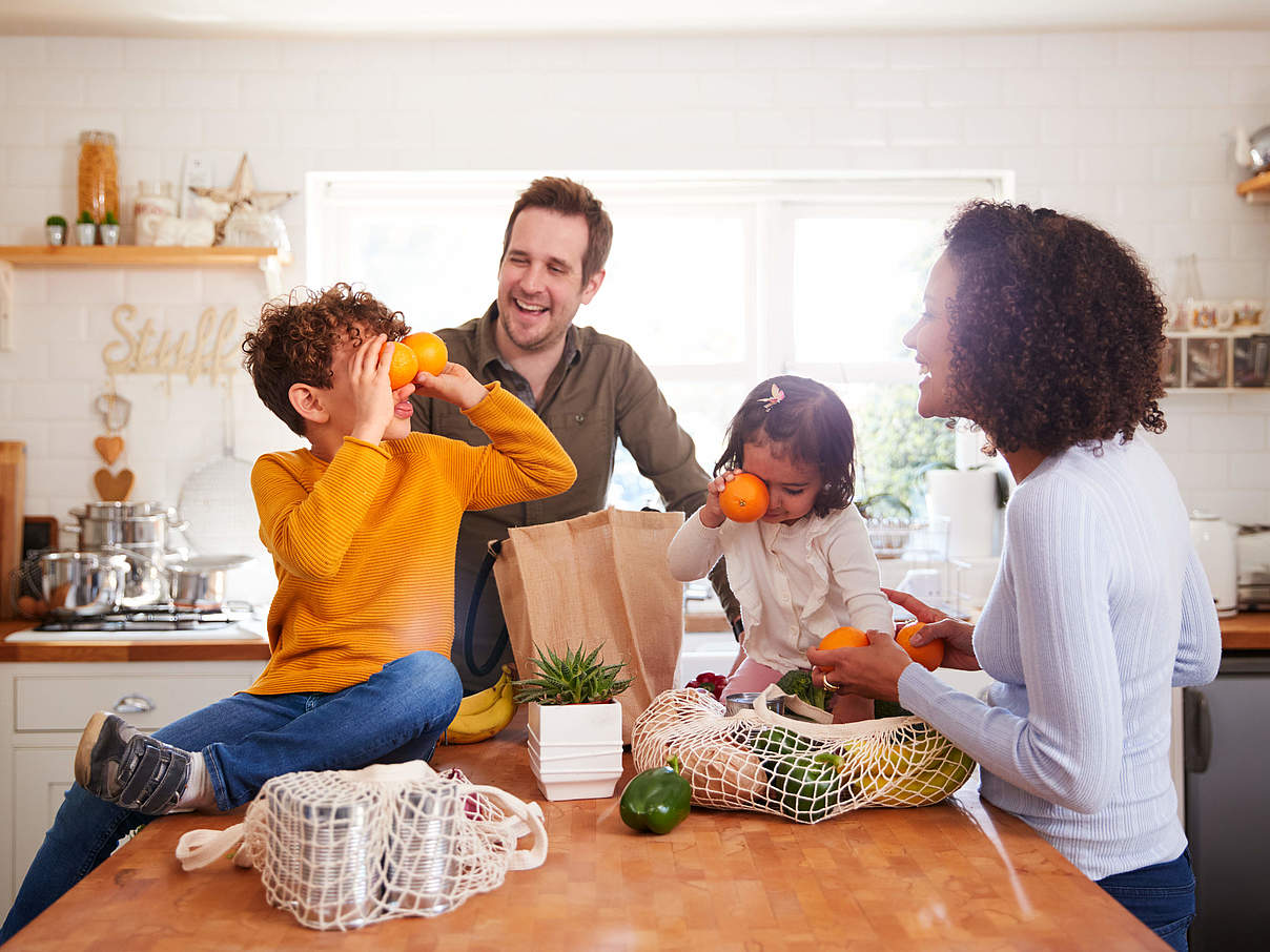 Family Returning Home From Shopping Trip Using Plastic Free Bags Unpacking Groceries In Kitchen