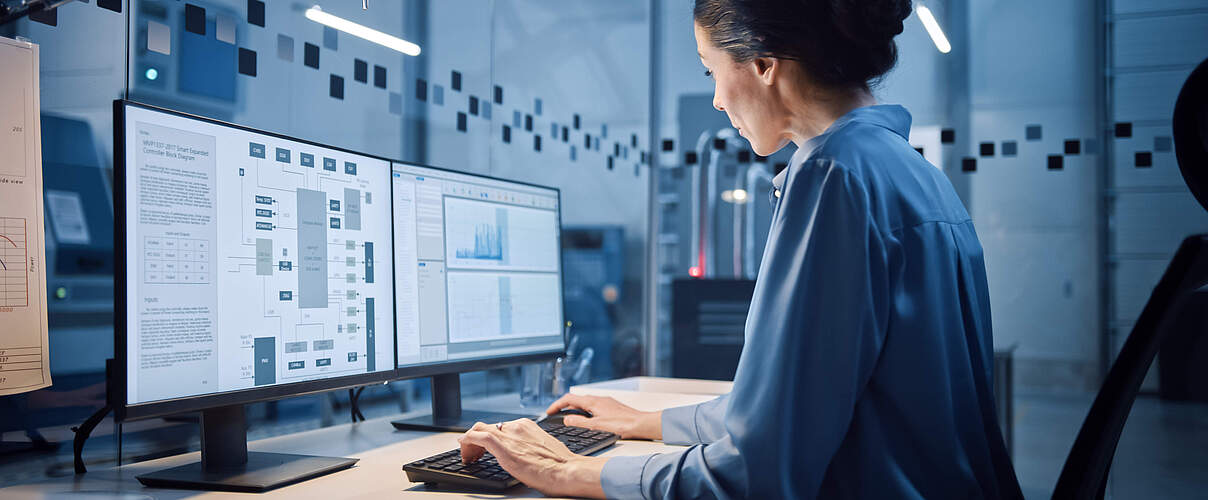 Factory Office: Portrait of Beautiful and Confident Female Industrial Engineer Working on Computer, on Screen Industrial Electronics Design Software. High Tech Facility with CNC Machinery