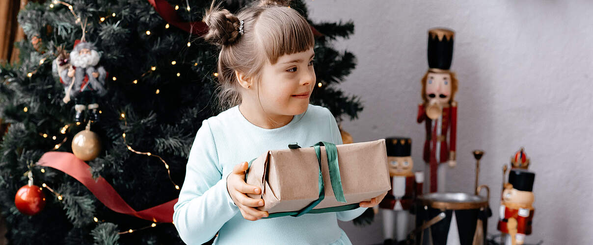 Mädchen mit einem Geschenk vor dem Weihnachtsbaum