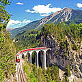 Bahn, die sich auf einem Viadukt durch eine grüne Berglandschaft schlängelt 