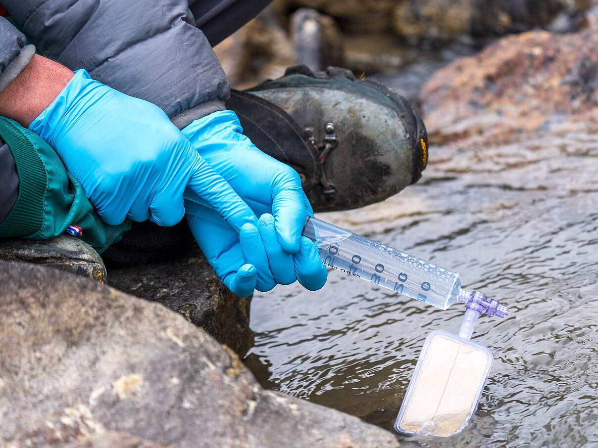 Hände mit Gummihandschuhen nehmen Wasserprobe per Spritze mit kleinem Filter