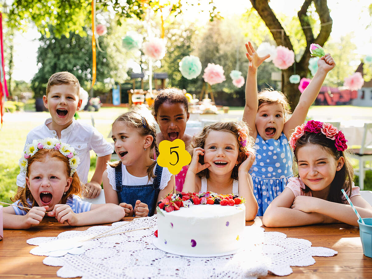 Kinder am Tisch sitzend feiern Geburtstag draußen