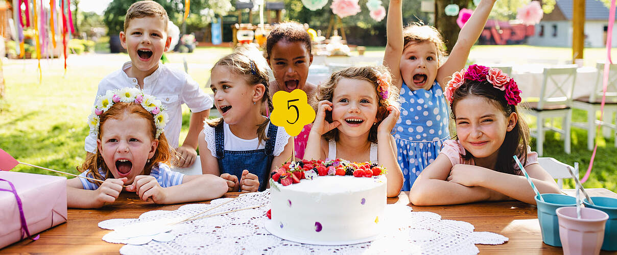 Kinder am Tisch sitzend feiern Geburtstag draußen