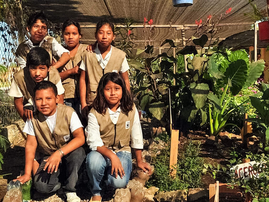 Sechs Kinder mit braunen Schul-Westen mit WWF-Symbol neben vielen grünen Pflanzen sehen in die Kamera
