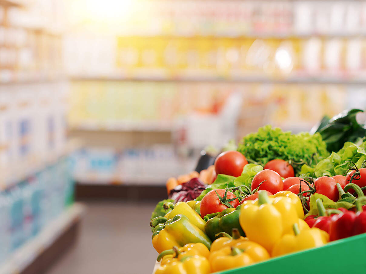 Symbolbild eines Supermarktes mit frischem Gemüse im Vordergrund und einem verschwommenen Hintergrund