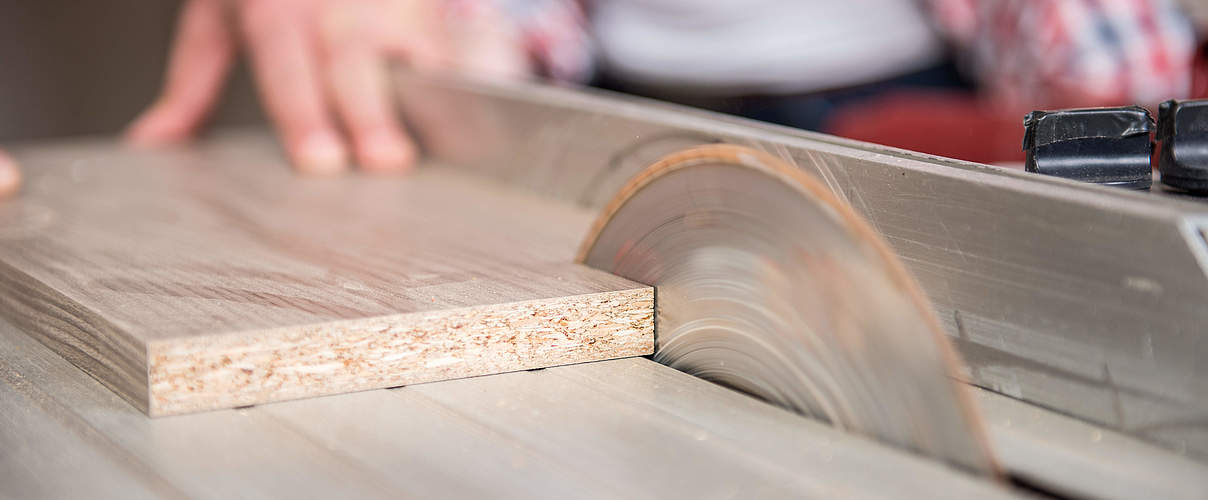 Woman and man using power tools in a carpenter workshop