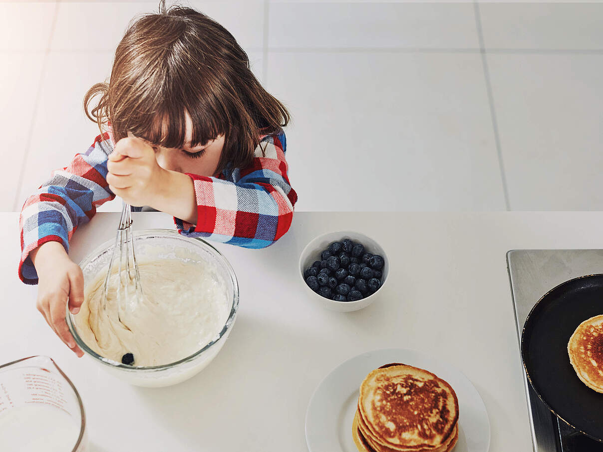 Kind rührt Teig für Blaubeer-Pfannkuchen 