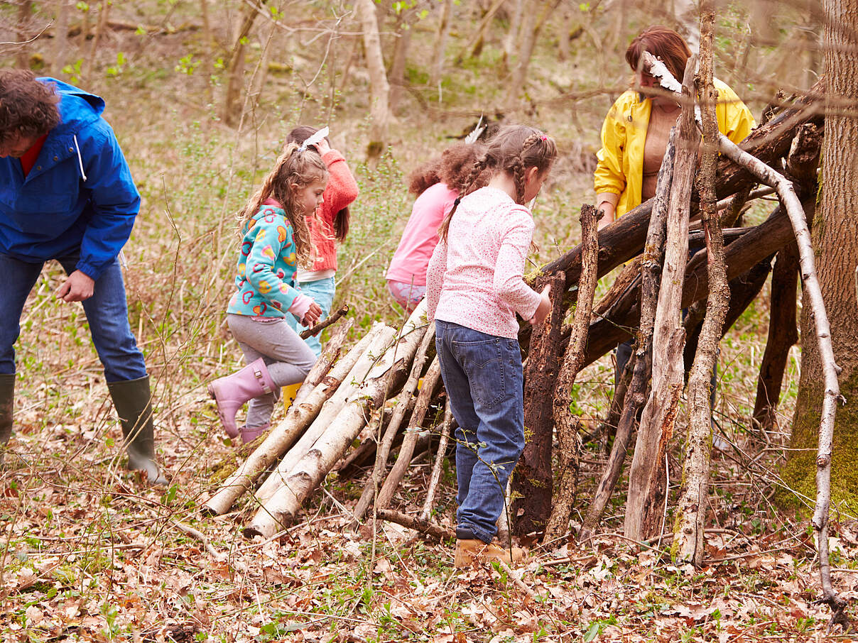 Kinder bauen zusammen mit Erwachsenen eine Waldhütte