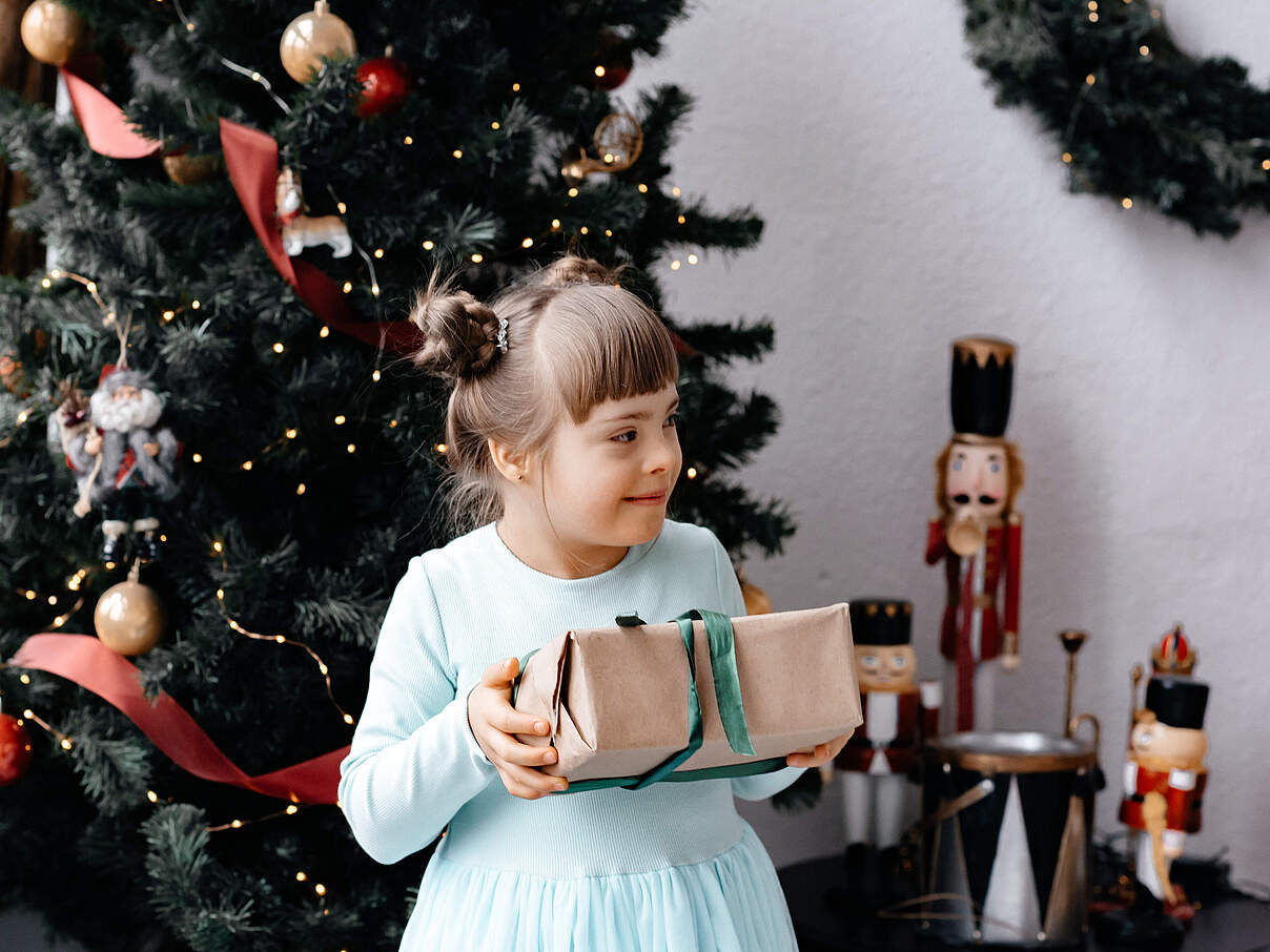 Mädchen mit einem Geschenk vor dem Weihnachtsbaum