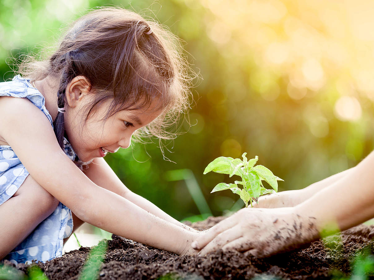 Kind pflanz mit Hilfe eine Pflanze in den Boden © Shutterstock / A3pfamily WWF