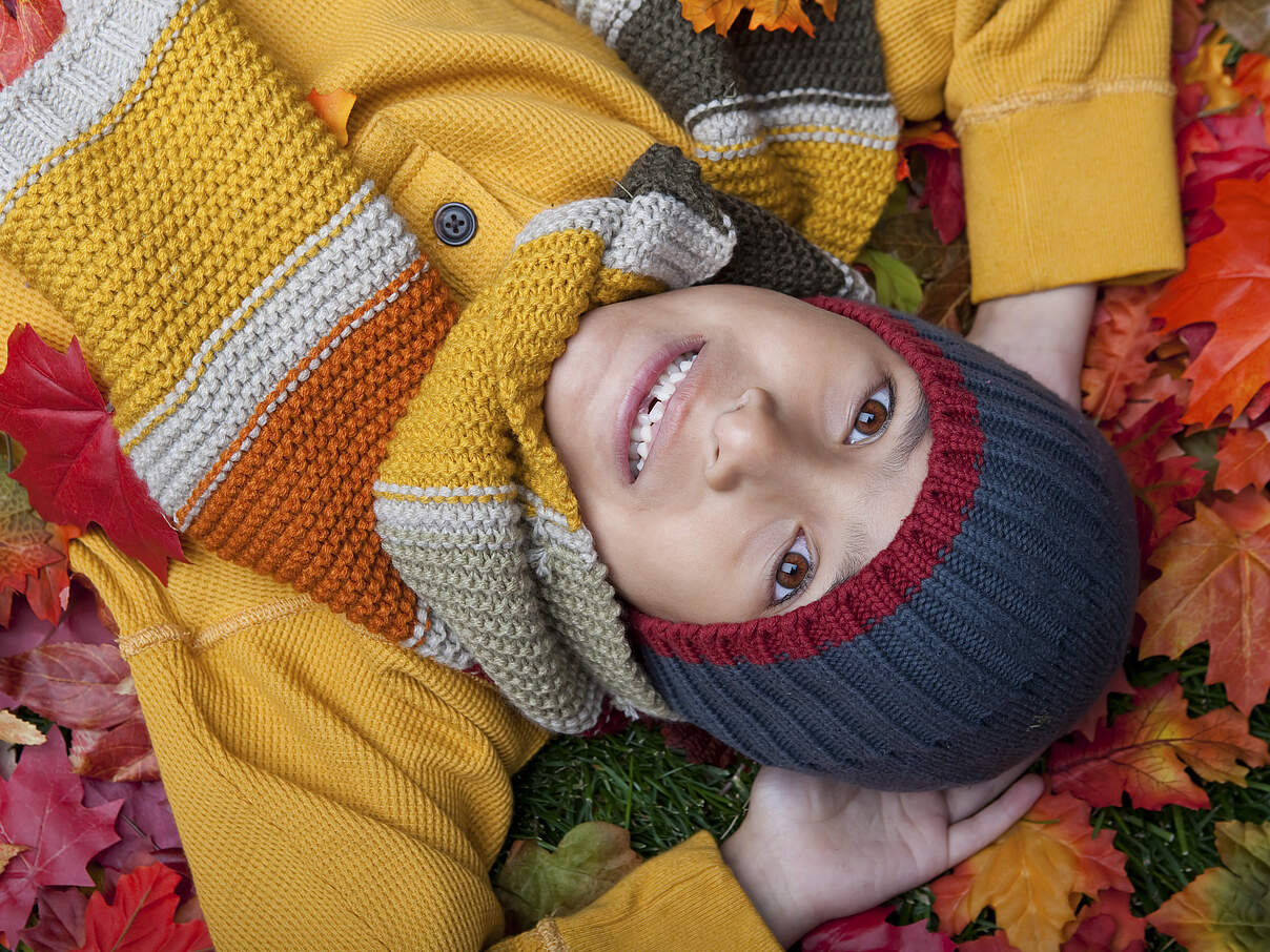 Kind mit buntem Wollschal und Wollmütze im Laub