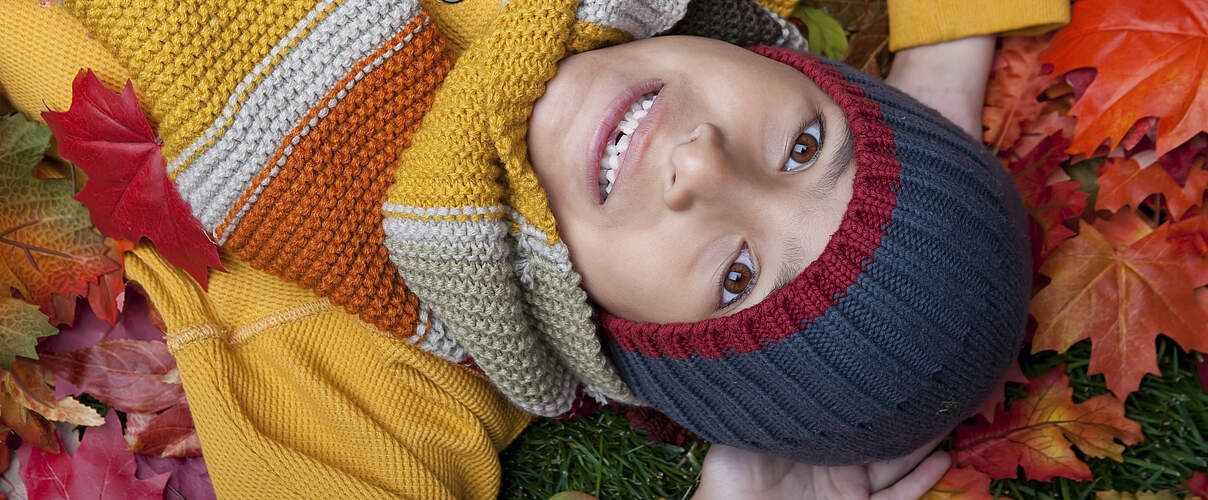 Kind mit buntem Wollschal und Wollmütze im Laub