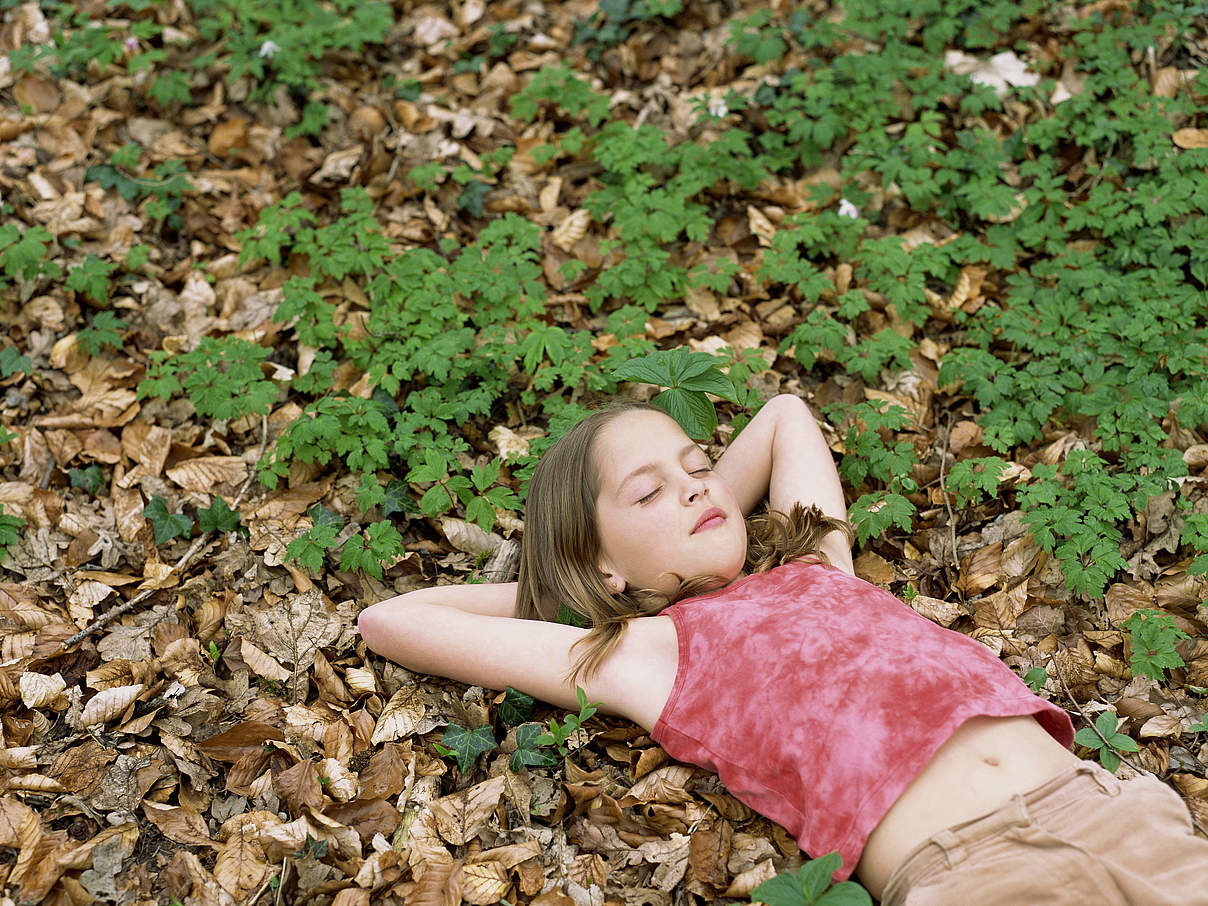 Ein Mädchen mit geschlossenen Augen liegt auf dem Waldboden. © Creatas Images / iStock / GettyImages