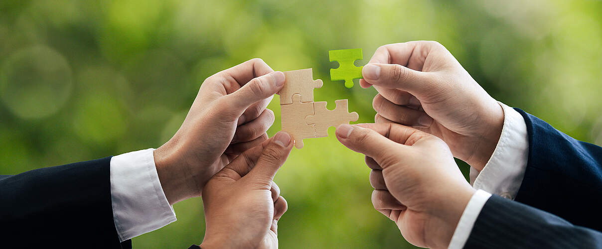 Office workers holding a jigsaw puzzle, teamwork and unity. Charity, volunteering, problem solving, business unity, business teamwork, success and strategy. Green background.
