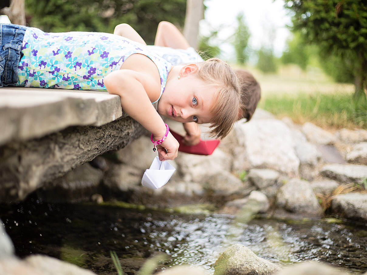Kind spielt am Wasser mit Papierschiff