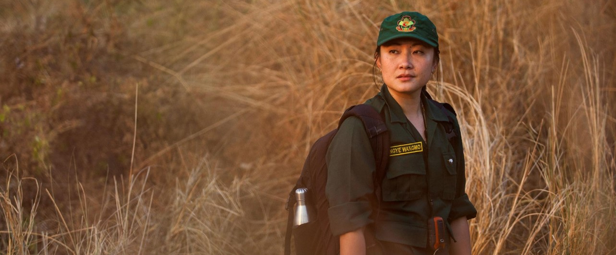 Rangerin in grüner Uniform mit Rucksack in Grassavanne
