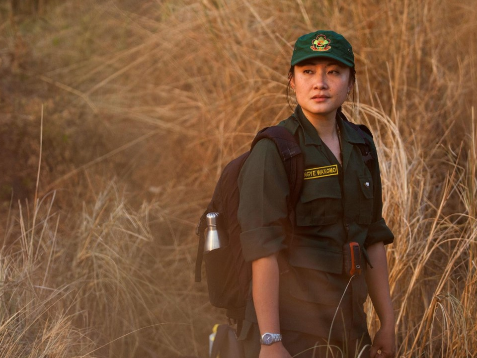 Rangerin in grüner Uniform mit Rucksack in Grassavanne