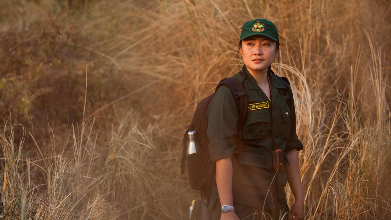 Rangerin in grüner Uniform mit Rucksack in Grassavanne