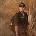 Rangerin in grüner Uniform mit Rucksack in Grassavanne