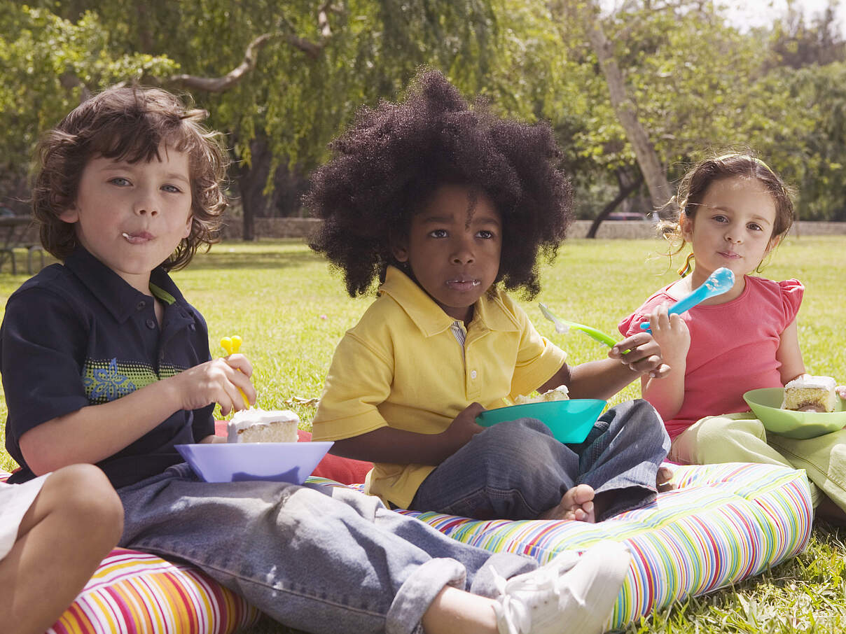 Kinder essen Kuchen im Park © GettyImages Kinder essen Kuchen im Park