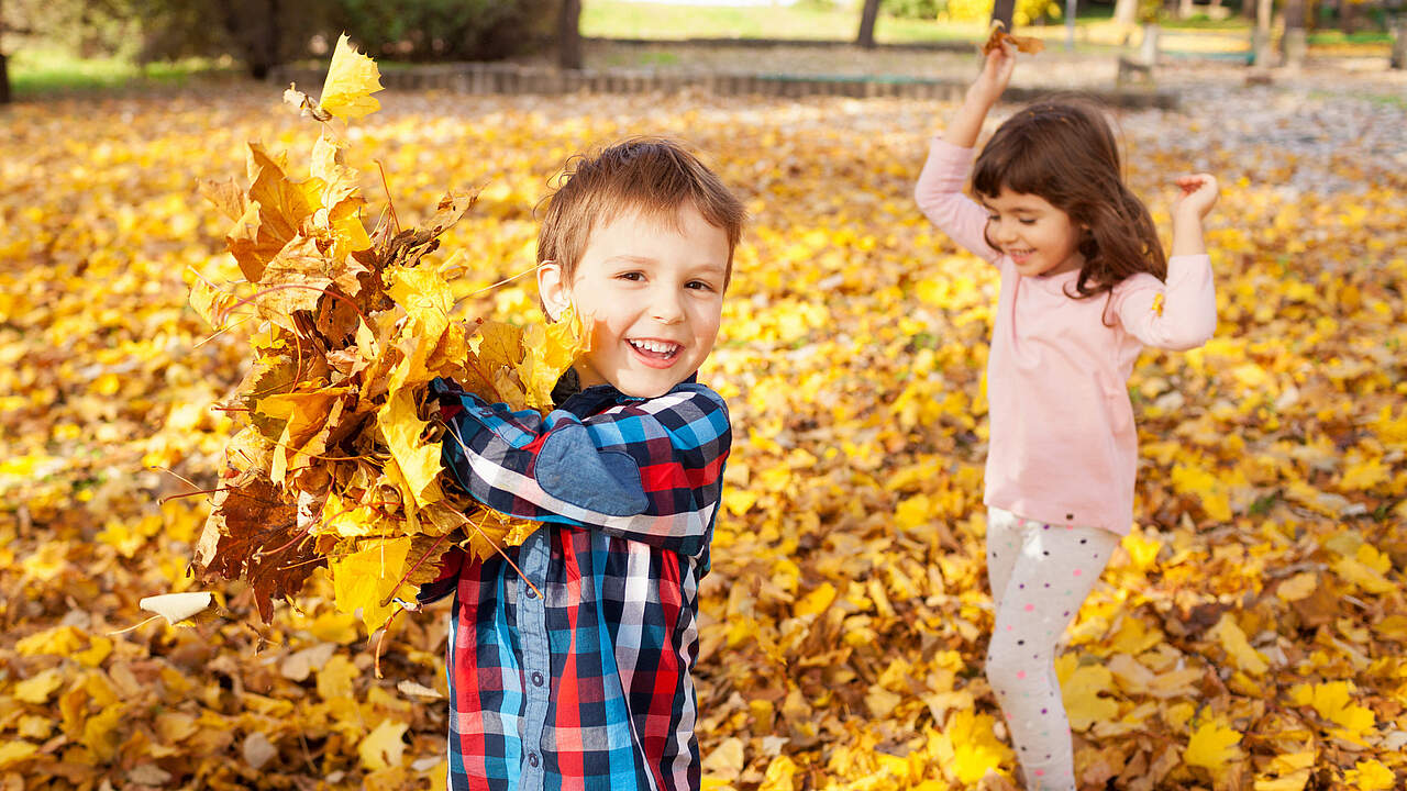 Kinder im Herbst spielen mit Blättern