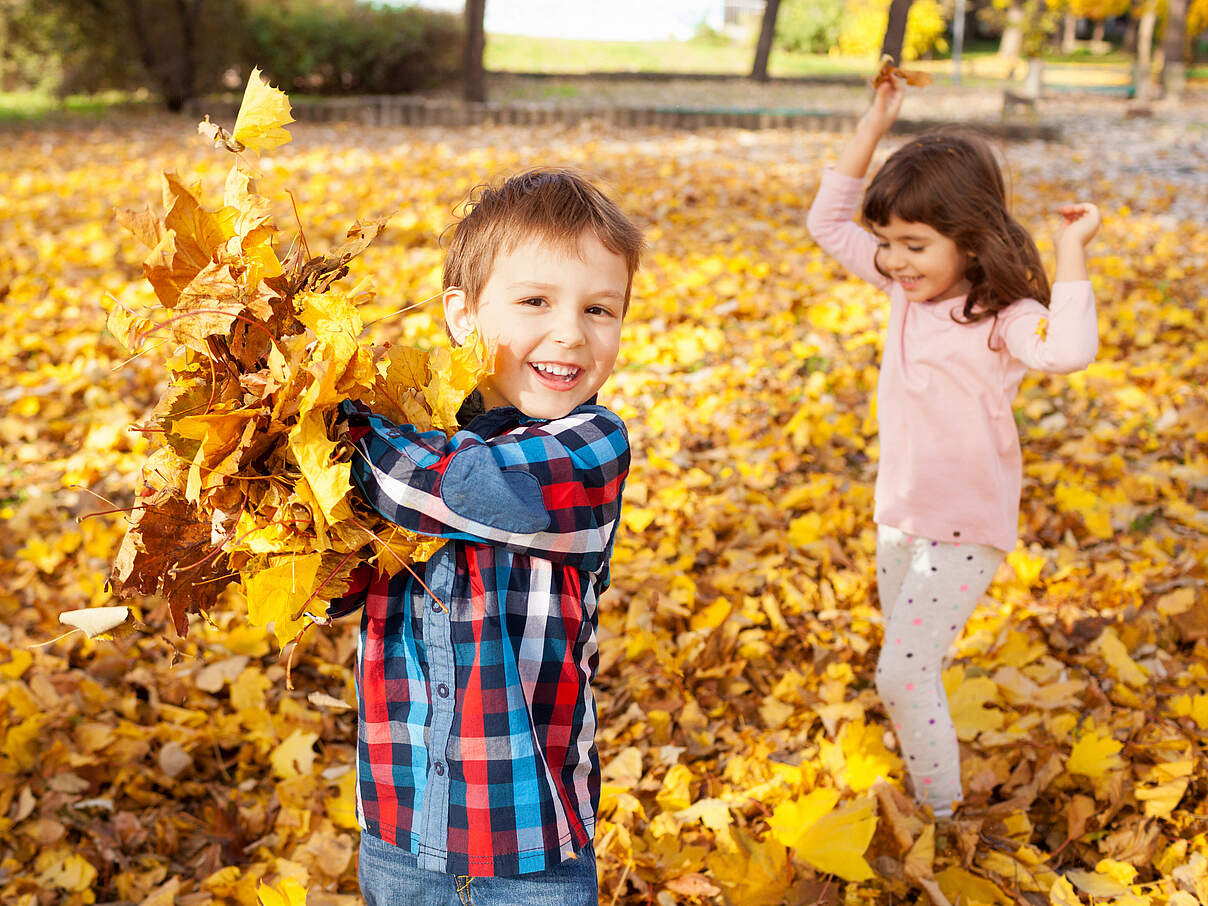 Kinder im Herbst spielen mit Blättern