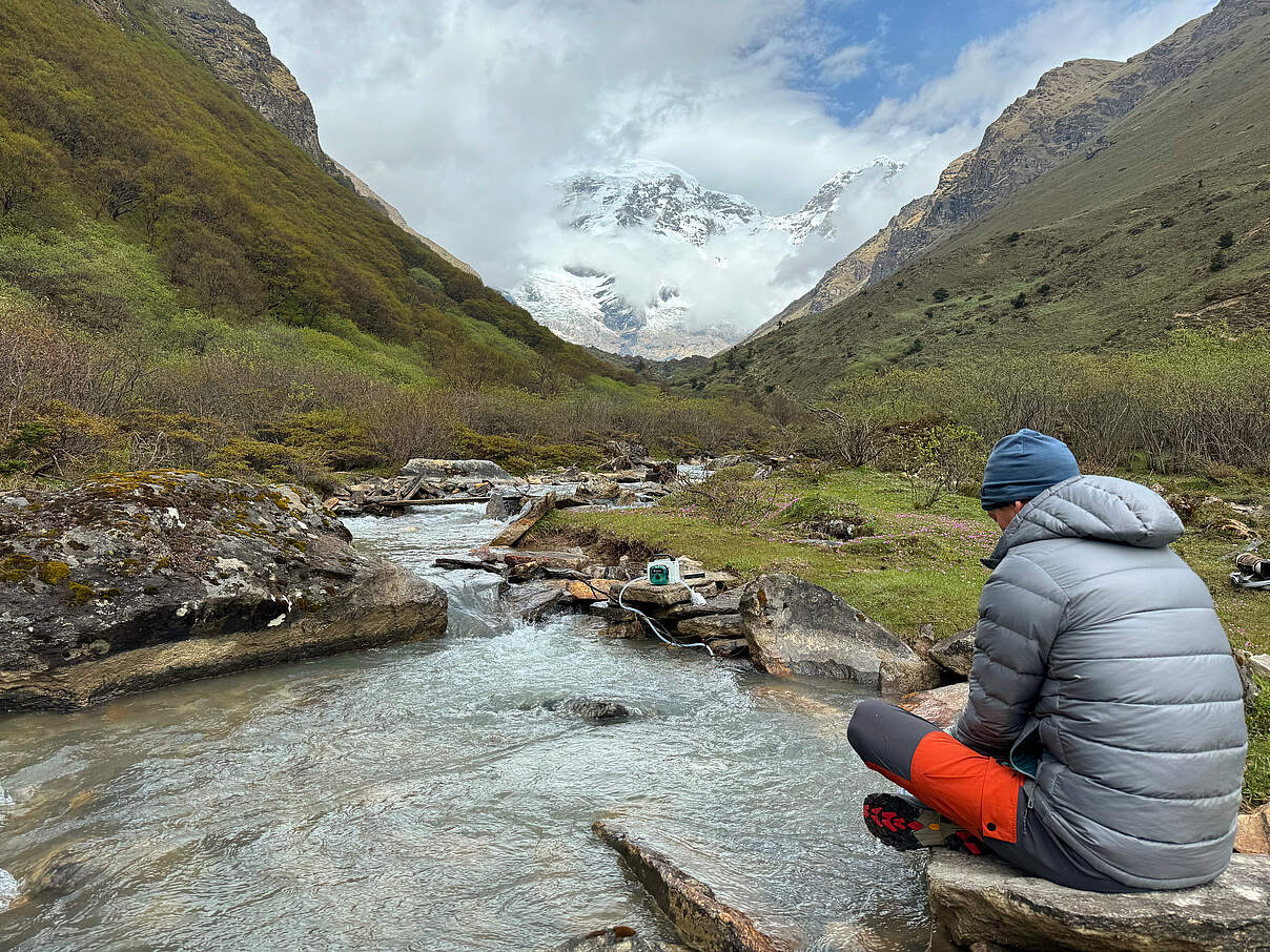Tolles Bergpanorama mit Gebirgsfluss. Ein Mann wartet, dass eine Pumpe ausreichend Wasser sammelt. 